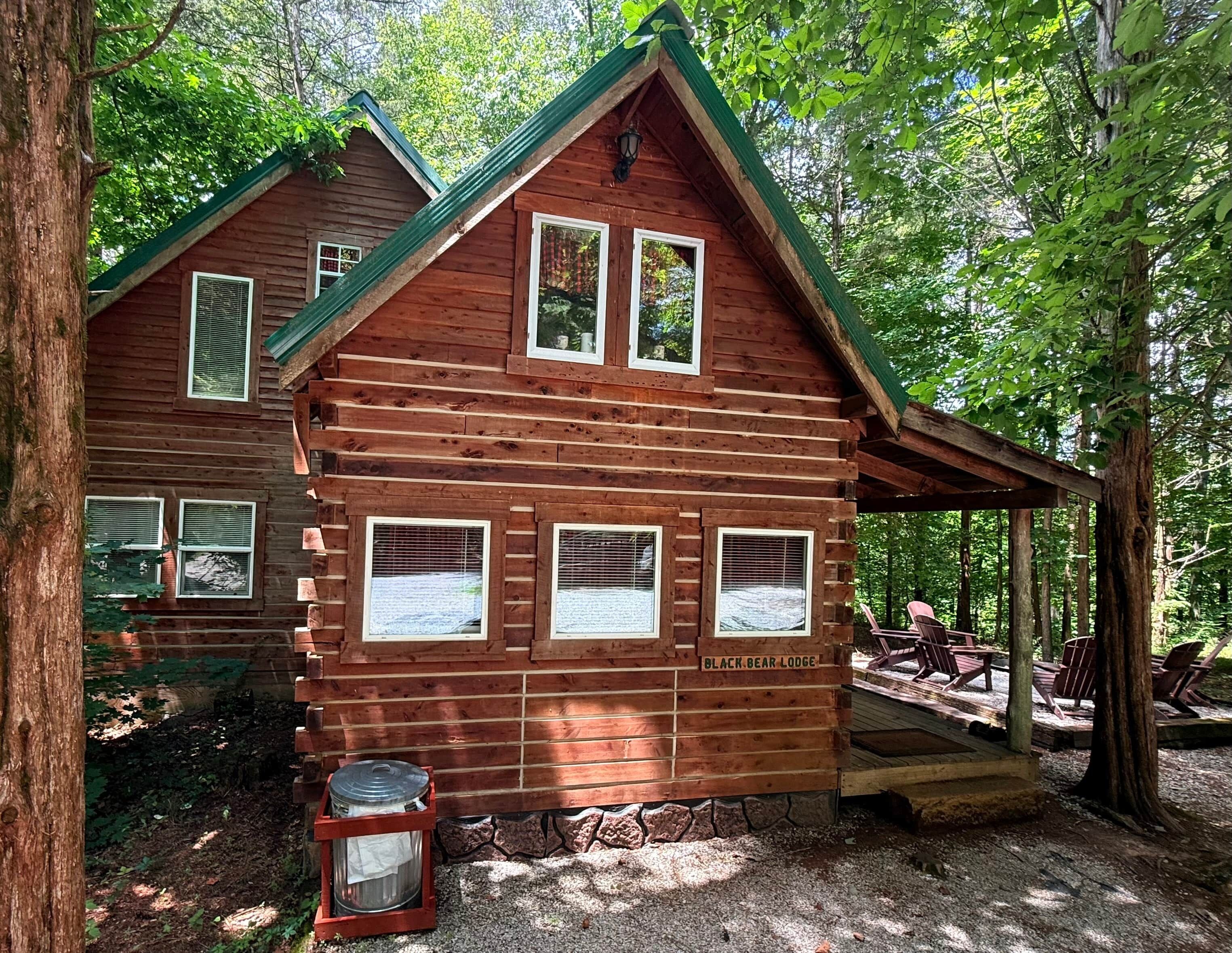 A log cabin with a green roof, multiple windows, and a sign reading 'BLACK BEAR LODGE'.