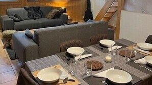 Un coin repas chaleureux avec un plafond en bois, un canapé et une table dressée pour quatre personnes.
