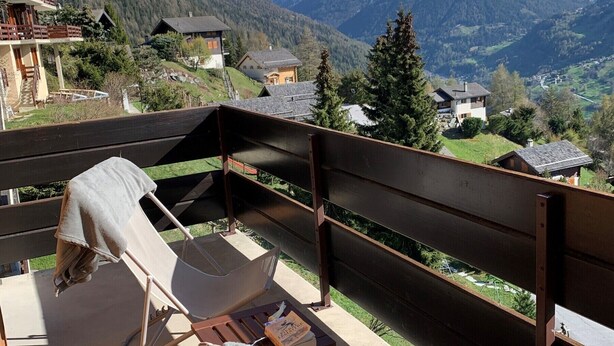 Un balcon offrant une vue sur des montagnes enneigées, un banc en bois et une serviette posée sur le banc.
