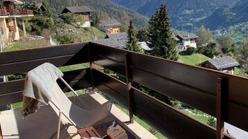 Un balcon offrant une vue sur des montagnes enneigées, un banc en bois et une serviette posée sur le banc.