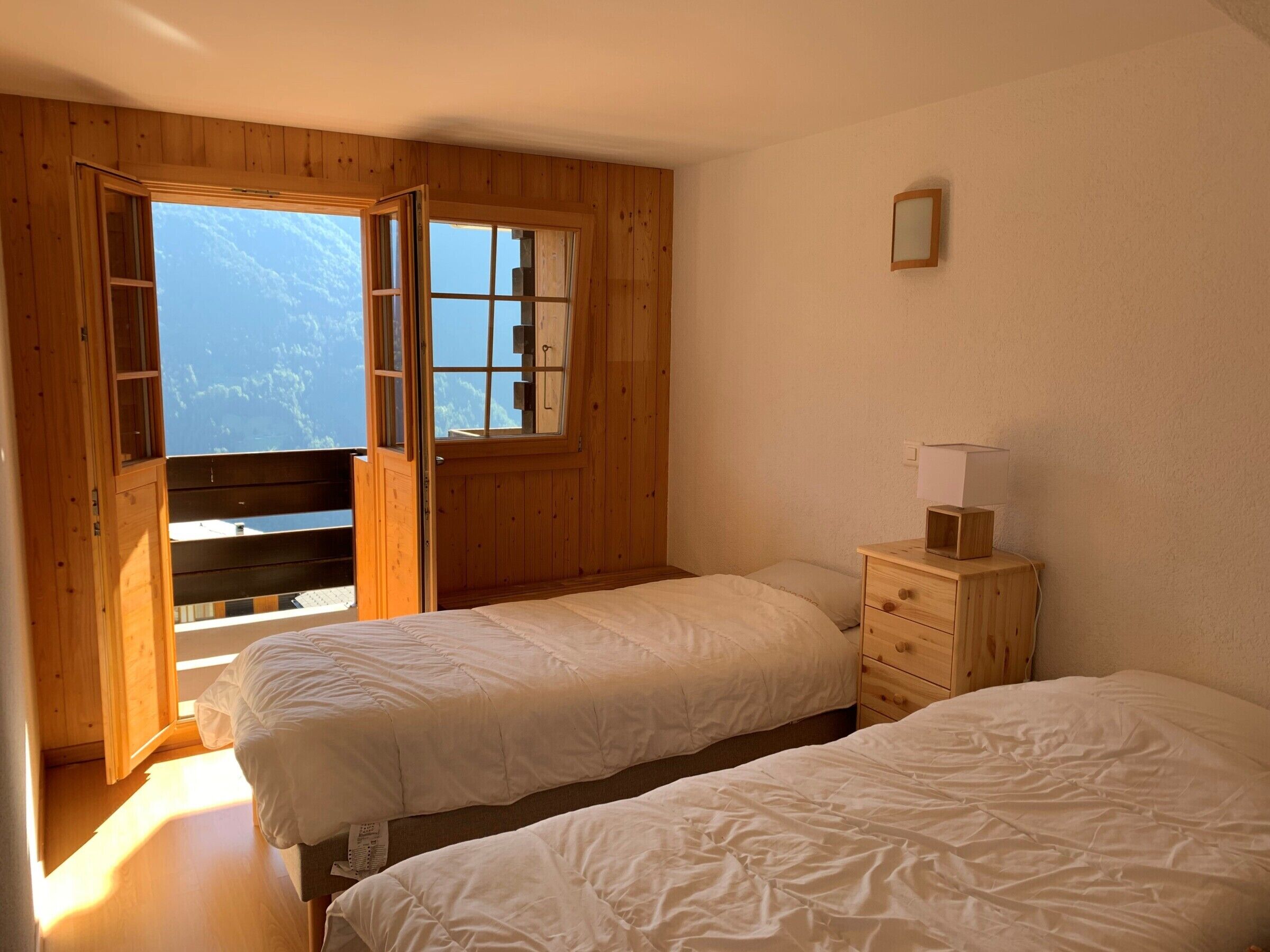 Une chambre avec deux lits, des murs en bois, une fenêtre et une table de chevet avec une lampe.