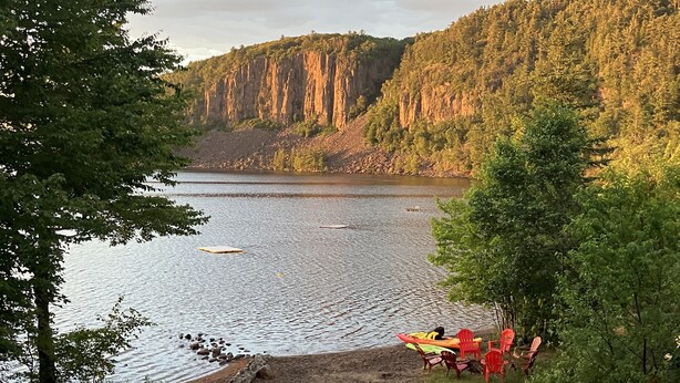 Une vue sur le lac, avec un kayak et des chaises au bord de l’eau.
