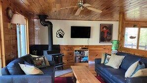 Un intérieur de chalet chaleureux avec une cheminée, deux canapés, une table basse en bois et une bibliothèque.