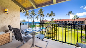 A balcony with a table and chairs, overlooking a pool and palm trees. - Spacious 3bd Papakea condo, the perfect getaway (Lahaina)