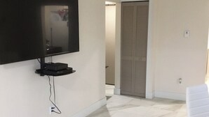 Un salon moderne avec un téléviseur à écran plat fixé au mur, un fauteuil blanc et un sol carrelé.
