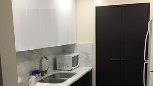 Une cuisine compacte avec un plan de travail blanc, un four à micro-ondes encastré, un évier et des meubles de rangement de couleur foncée.