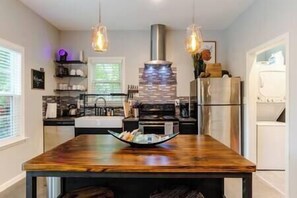 A modern kitchen with a central island, pendant lights, and a stainless steel range hood.