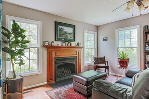 A living room with a fireplace, a large plant, a sofa, and a bookshelf. - The Pond Cabin: Hot Tub & Stocked Pond (Linden)