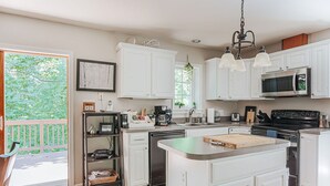 Una cocina con armarios blancos, una isla central, un microondas, una estufa y una cafetera.
