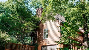 A wooden house with a garage, surrounded by lush greenery and a wooden fence. - The Pond Cabin: Hot Tub & Stocked Pond (Linden)