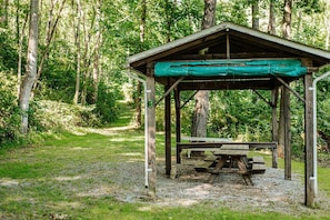 Un pavillon en bois avec une table de pique-nique, situé dans une zone boisée.