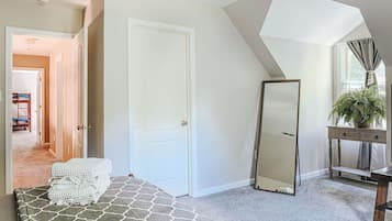 A bedroom with a stone-patterned bed, a large mirror, a potted plant, and a view of a hallway.