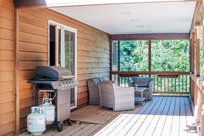 Une terrasse en bois avec un barbecue, deux fauteuils en osier et une table.