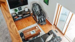 A living room with a TV, massage chair, sofa, and a coffee table. - The Pond Cabin: Hot Tub & Stocked Pond (Linden)