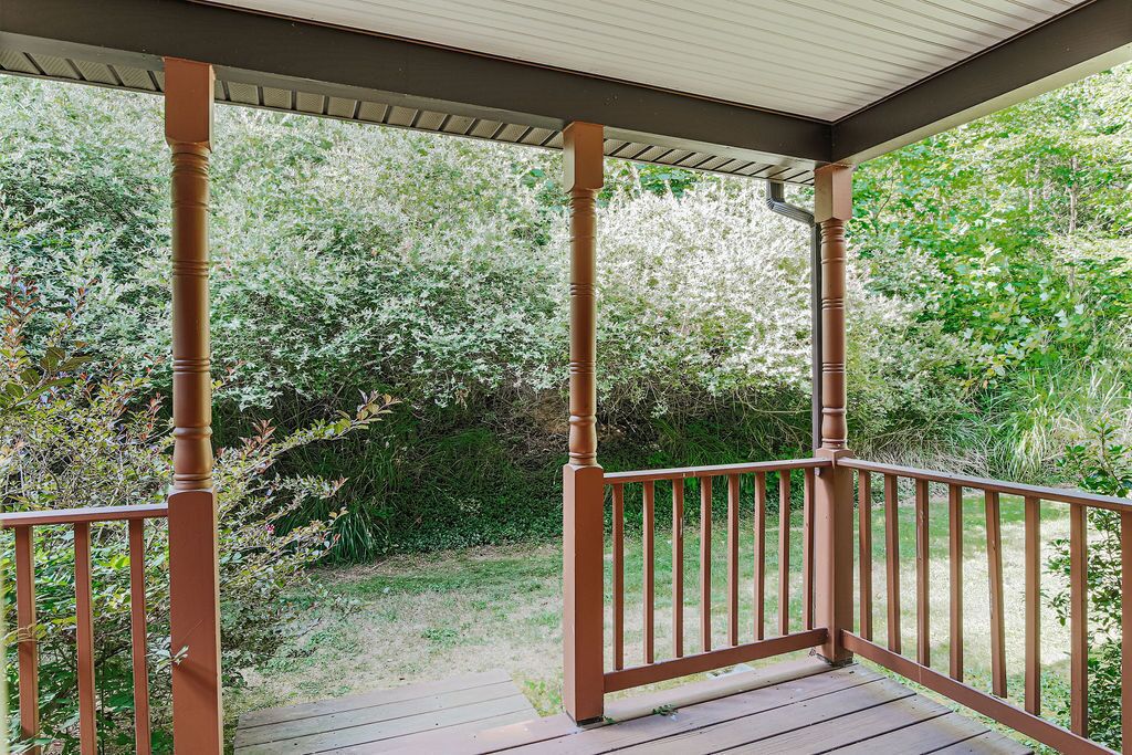 A covered porch with wooden railings and a view of a garden.