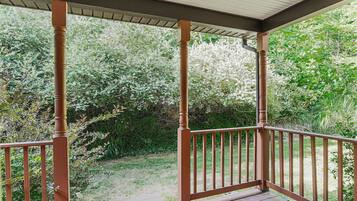 A covered porch with wooden railings and a view of a garden.