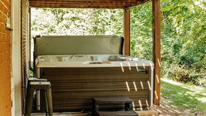 Un jacuzzi bajo una pérgola de madera, con un muro de ladrillo y follaje al fondo.