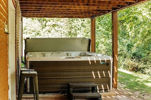 Un bain à remous sous une pergola en bois, avec un mur en briques et de la verdure en arrière-plan.