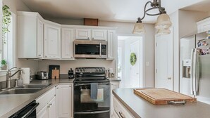 A kitchen with white cabinets, a stainless steel microwave, a black oven, and a wooden cutting board on the counter. - The Pond Cabin: Hot Tub & Stocked Pond (Linden)