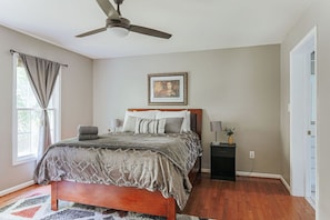 A bedroom with a bed, a ceiling fan, a bedside table with a lamp, and a framed picture on the wall.