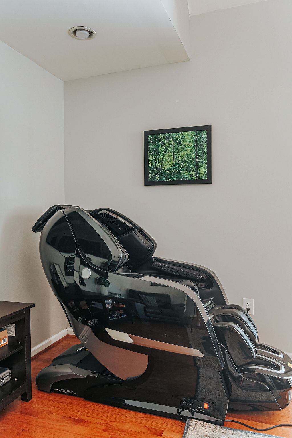 A massage chair in a room with a framed picture on the wall and a wooden floor.