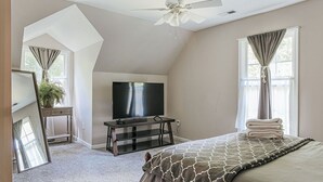A bedroom with a bed, a TV on a stand, a ceiling fan, and a window with curtains. - The Pond Cabin: Hot Tub & Stocked Pond (Linden)