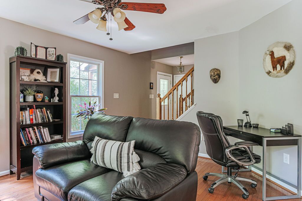 A living room with a leather sofa, a bookshelf, a desk with a chair, and a staircase.