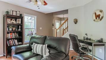 A living room with a leather sofa, a bookshelf, a desk with a chair, and a staircase.