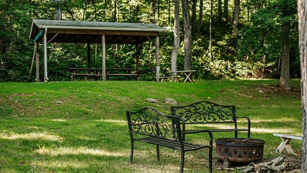 A park with a metal bench, a fire pit, and picnic tables under a shelter. - The Pond Cabin: Hot Tub & Stocked Pond (Linden)