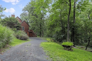 A house surrounded by a forested area with a gravel path leading to the entrance. - The Pond Cabin: Hot Tub & Stocked Pond (Linden)