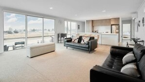 A spacious living area with a large window, a sofa, a coffee table, and a kitchen in the background.