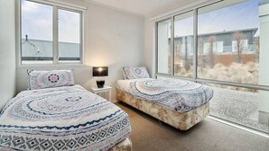 A bedroom with two beds, large windows, and a view of the outside.