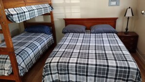 A room with two bunk beds and a single bed, all with plaid bedding. There is a wooden nightstand with a lamp and a wall-mounted electrical outlet. - Big Mountain Cabins with direct access to Windrock ATV Park (OLIVER SPRINGS)