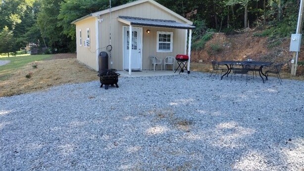 A small, single-story building with a gravel driveway, a barbecue grill, and a table with chairs. - Big Mountain Cabins with direct access to Windrock ATV Park (OLIVER SPRINGS)