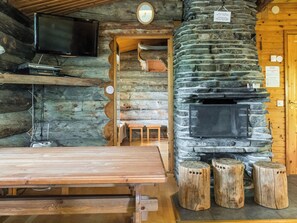 L’intérieur d’un chalet rustique, avec une cheminée en pierre, des bancs en bois et un téléviseur fixé au mur.