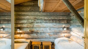 Een eenvoudig, landelijk ingericht blokhutinterieur met twee houten bedden, een klein tafeltje en twee wandlampen.