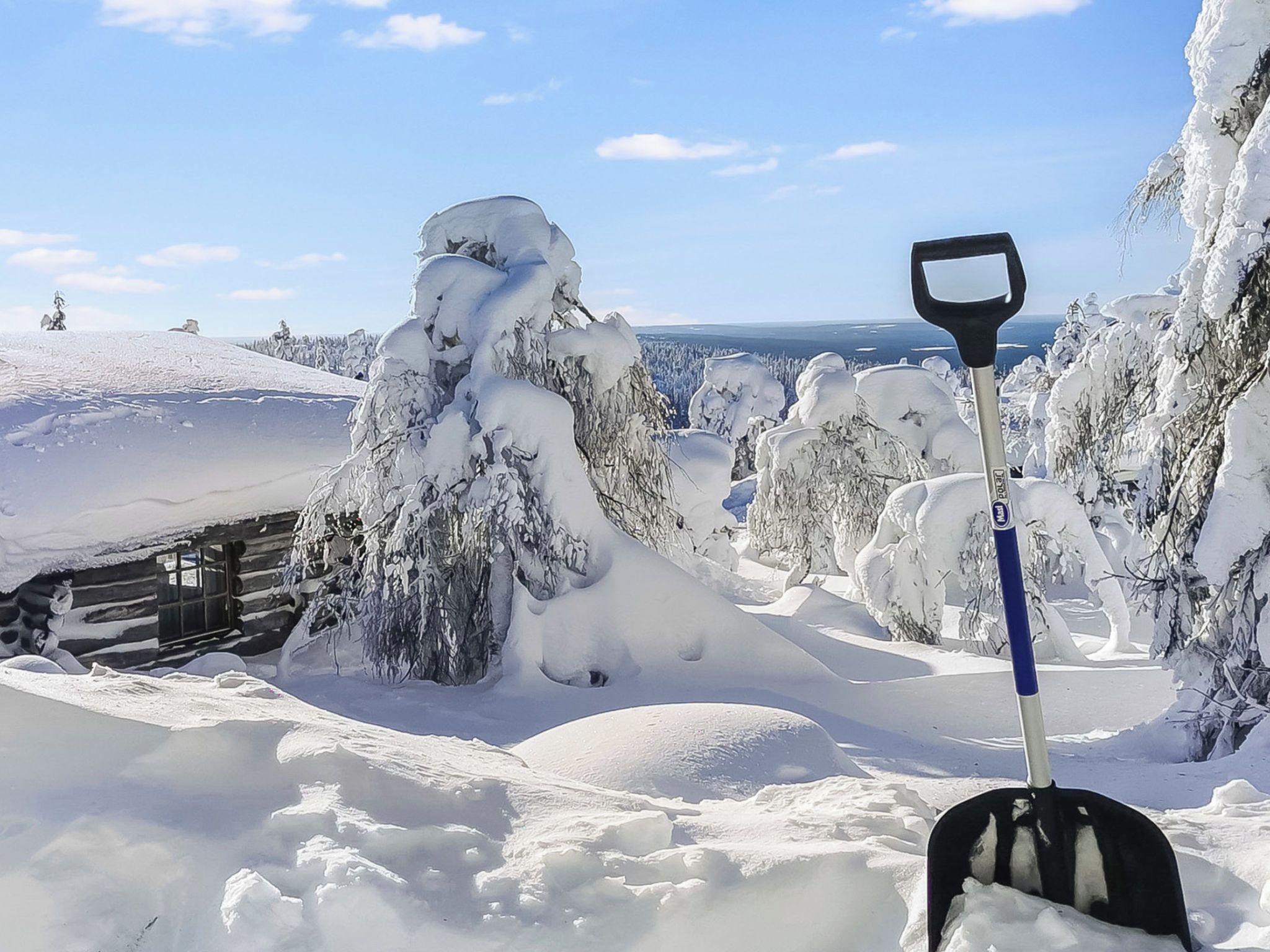 Paesaggio innevato con una baita di legno e una pala in primo piano.