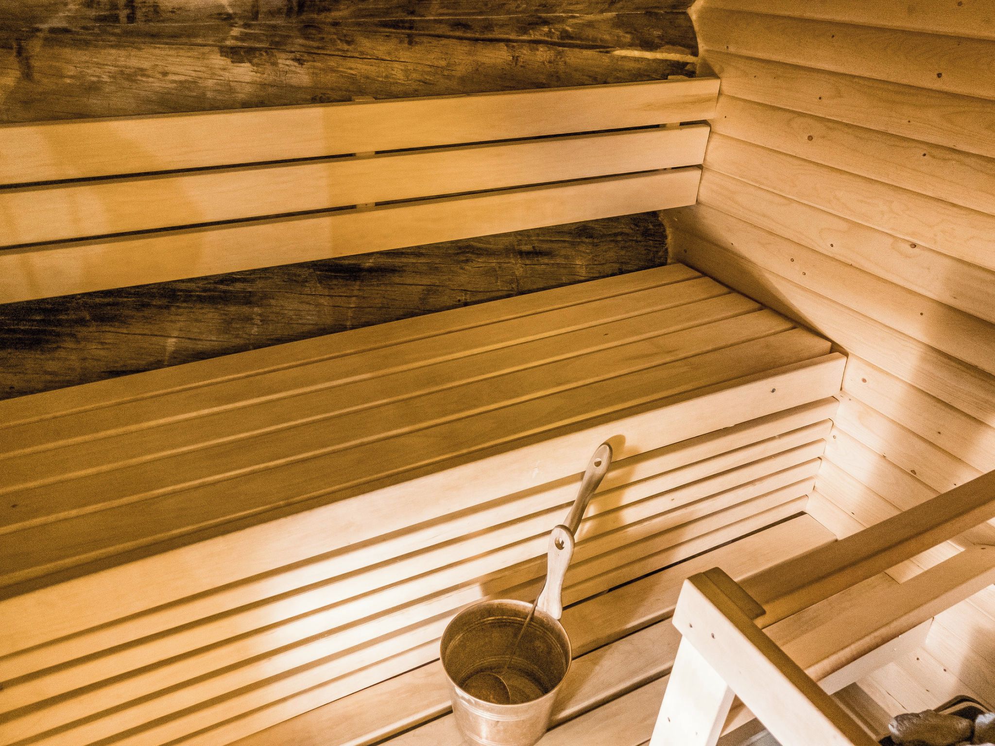 A sauna with wooden benches and a metal bucket.