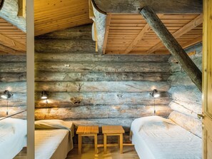A log cabin room with two beds, a small table, and two wall-mounted lamps. - Vilkkuna 20 a by Interhome (Pudasjärvi)