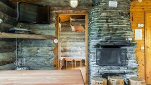 Een rustiek houten interieur met een stenen open haard, houten meubels en een aan de muur bevestigde televisie.