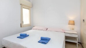 Ein kleines, sauberes Zimmer mit einem Einzelbett, einem Nachttisch mit Lampe und einem Fenster mit Vorhang.