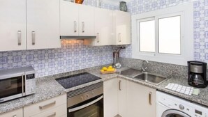 Eine kleine Küche mit weißen Schränken, einer Mikrowelle, einem Backofen, einem Spülbecken und einem Fenster.