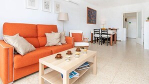 Ein helles Wohnzimmer mit einer Couch, einem Couchtisch und einem Essbereich mit Stühlen und einem Tisch.