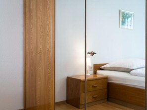 A bedroom with a wooden wardrobe, a bedside table with a lamp, and a bed with white bedding. - Panoramablick (A1001) by Interhome (Lahnstein (Koblenz))