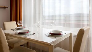 Une table à manger dressée avec des assiettes, des verres et des couverts, dans une pièce offrant une vue à travers de fines rideaux.