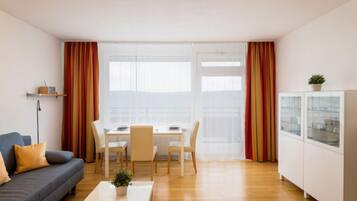 En moderne stue med sofa, sofabord, spisebord med stole og et køkken med skabe.
