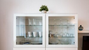 Un meuble blanc avec des portes en verre, contenant de la vaisselle et des verres blancs.