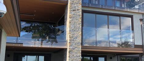 Una casa moderna de dos pisos con piscina, mobiliario exterior y un pilar de piedra.