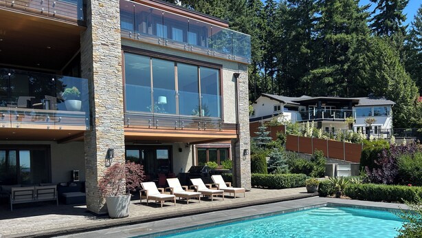 Una casa moderna con piscina, mobiliario exterior y fachada de piedra.