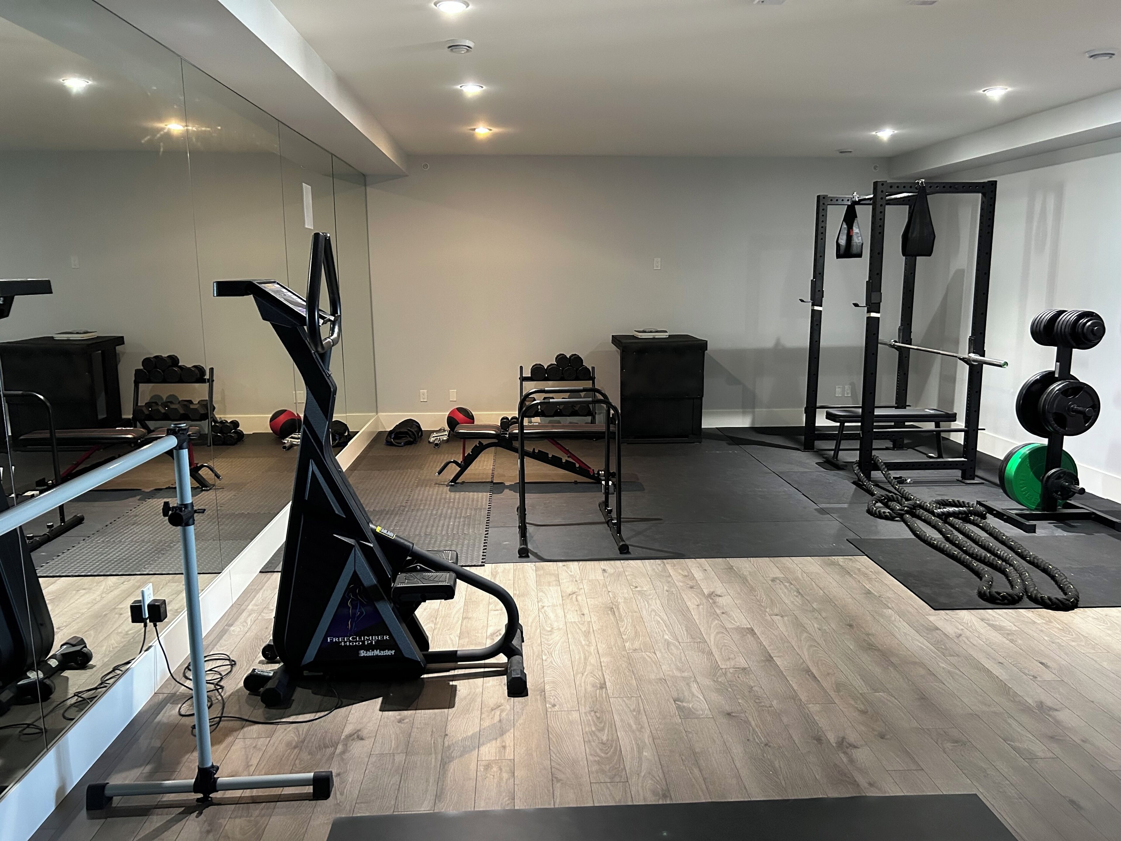A gym with exercise equipment, a mirror, and a wooden floor.